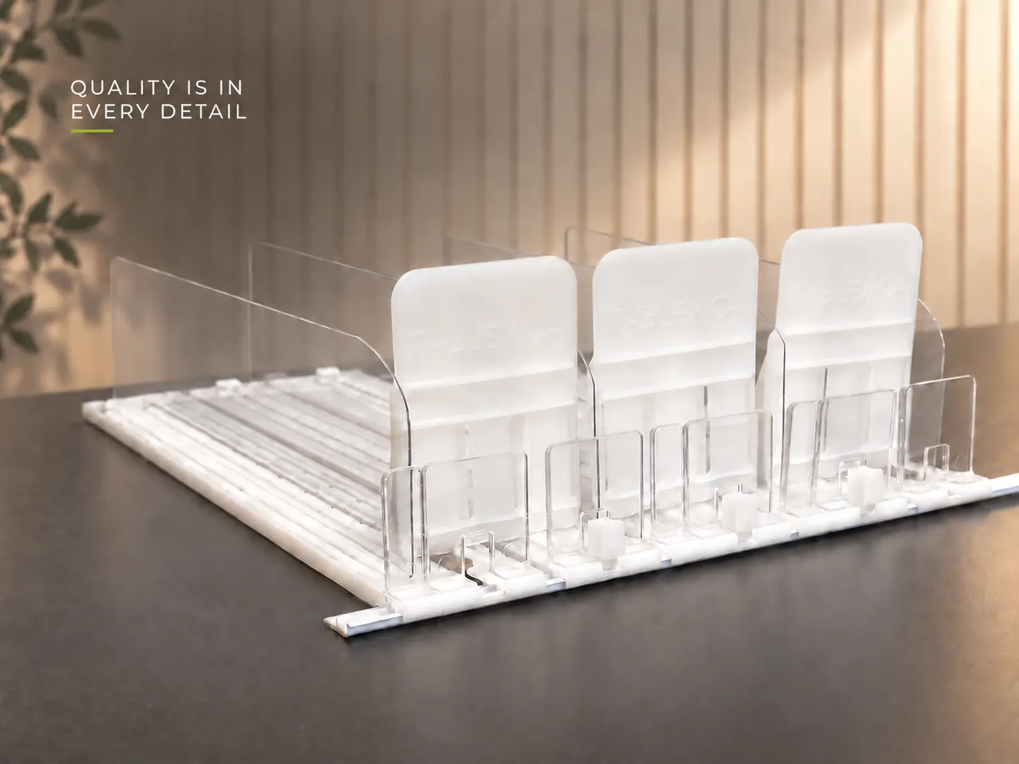 PRESTIGE shelf pusher system in place | Concept P.O.S. White multi-lane Prestige assembly on a dark counter: opaque pusher paddles, clear dividers and low front stops